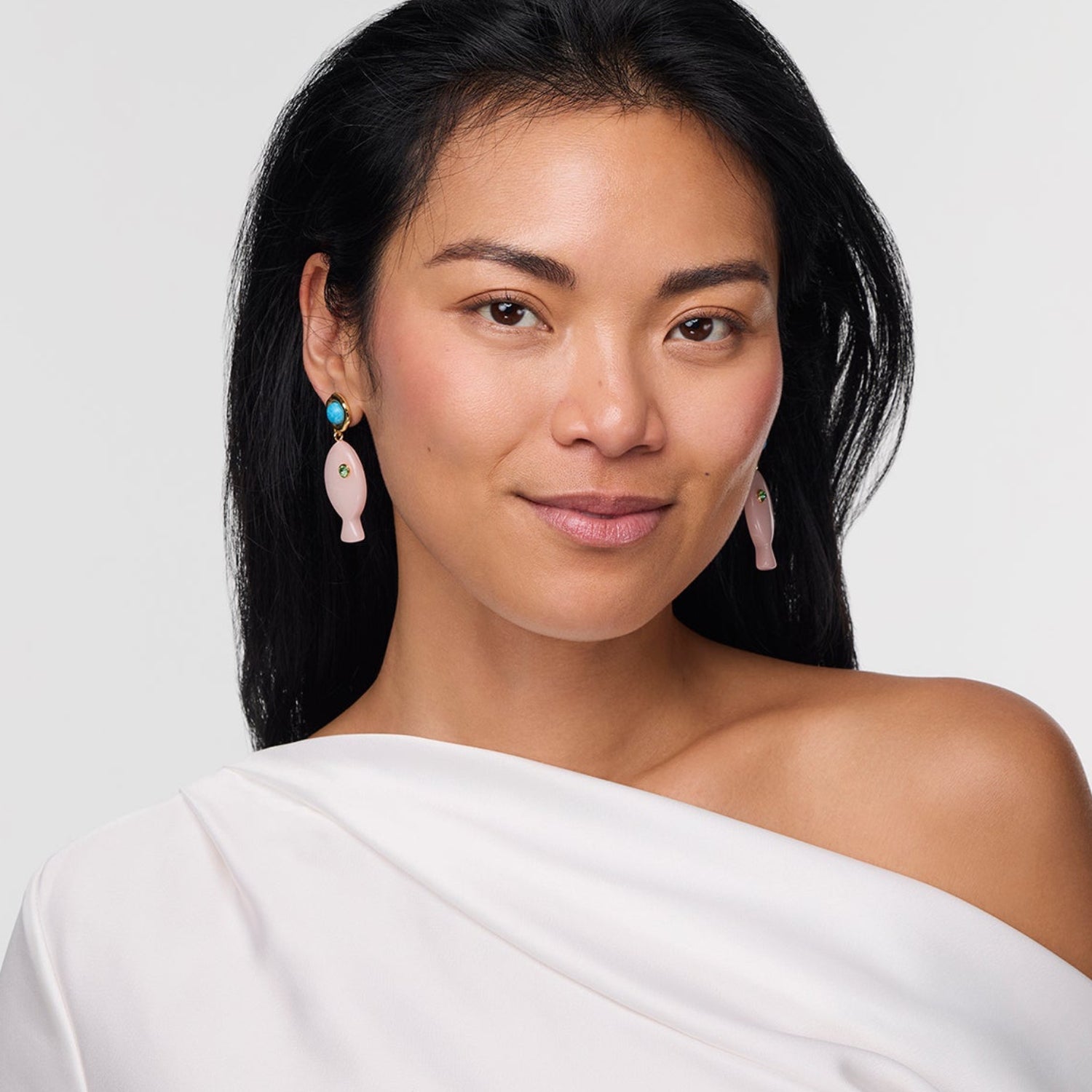 Woman wearing a white off-shoulder top with pink earrings on a light gray background