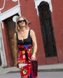 Woman in a black polka dot top and colorful pants walking on a street showing off a gold chain necklace with pink and stone charms