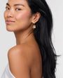 Woman with a ponytail wearing gold earrings against a plain background