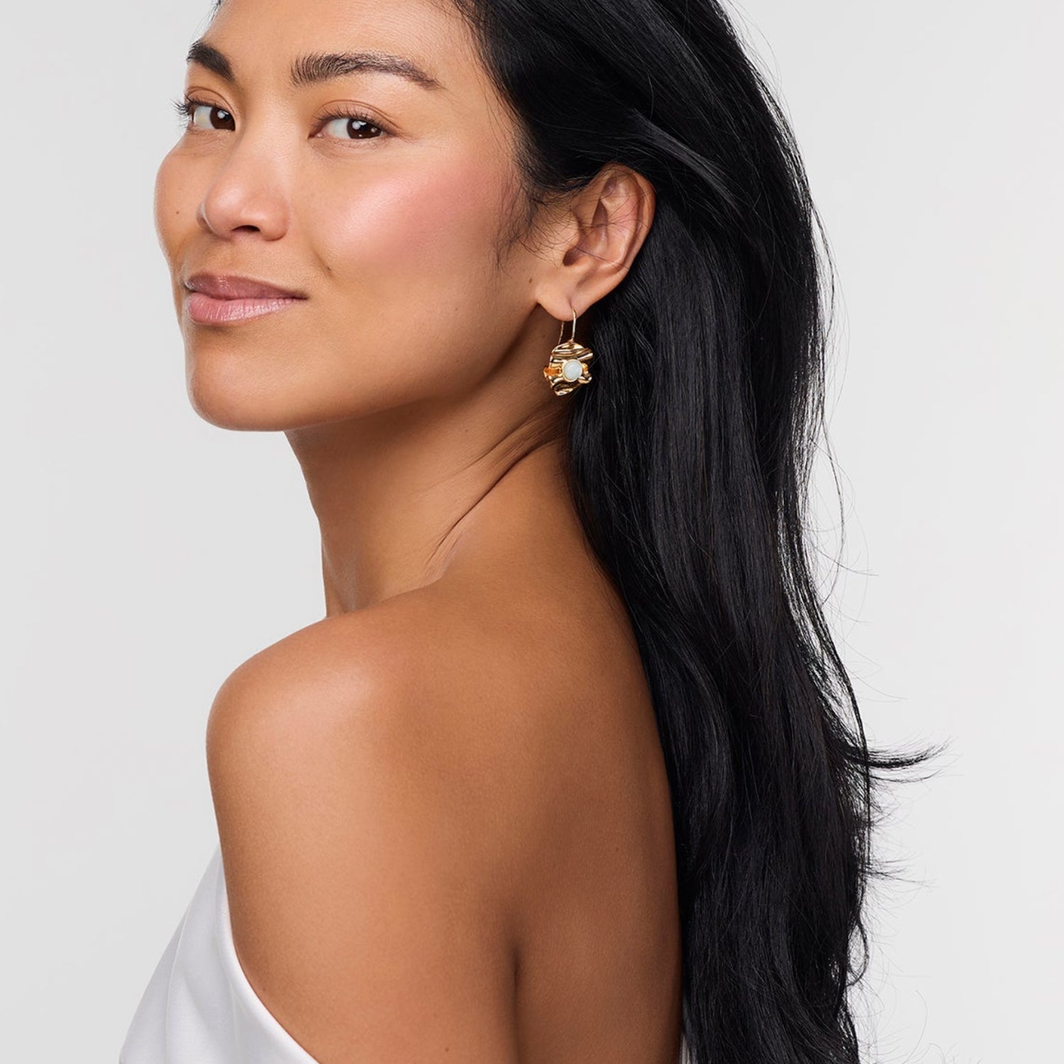 Woman with a ponytail wearing gold earrings against a plain background