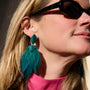 Teal feather drop earrings with gold-tone and green beaded details on Mignonne Gavigan close up 