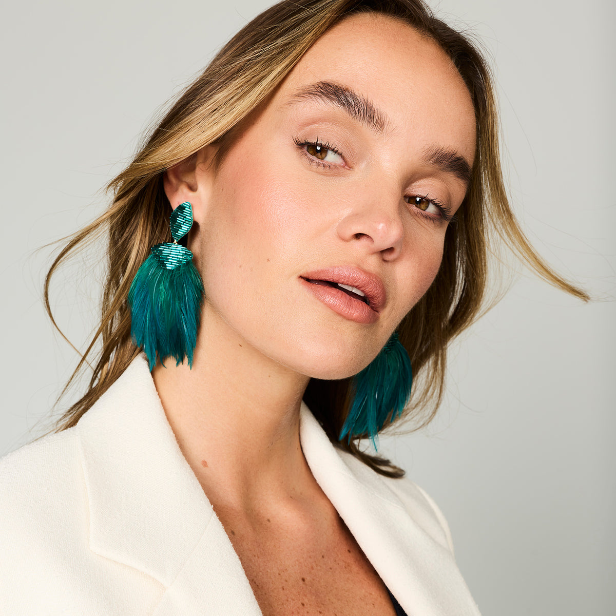 Teal feather drop earrings with gold-tone and green beaded details on model close up