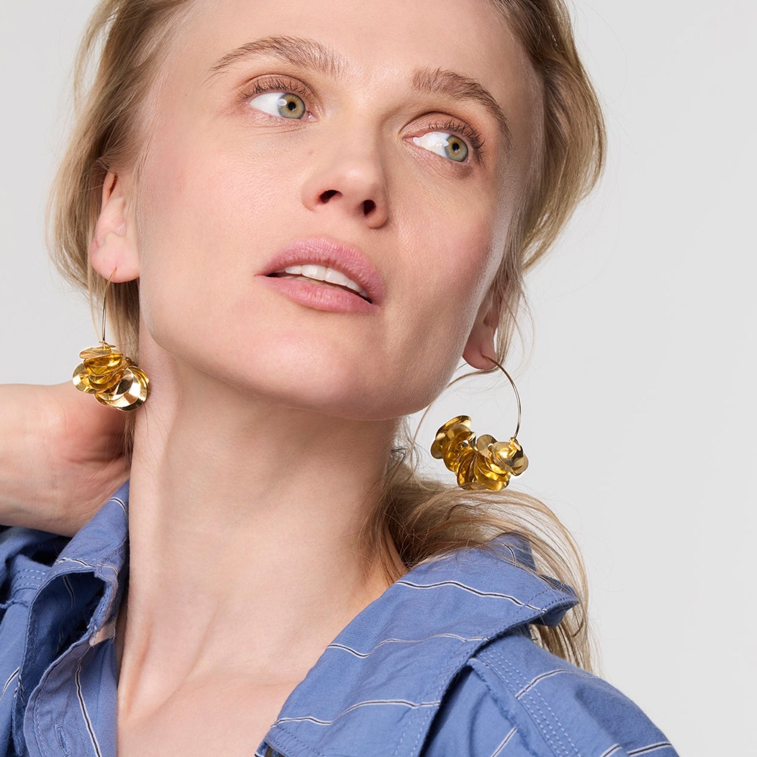 Woman wearing gold earrings with a plain background