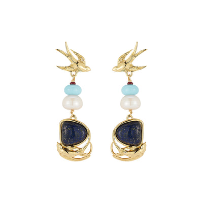 A pair of gold-tone dangle earrings featuring a swallow motif at the top, accented with light blue and white beads, and a large dark blue lapis lazuli-style stone in a wave-like gold setting at the bottom.