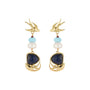 A pair of gold-tone dangle earrings featuring a swallow motif at the top, accented with light blue and white beads, and a large dark blue lapis lazuli-style stone in a wave-like gold setting at the bottom.
