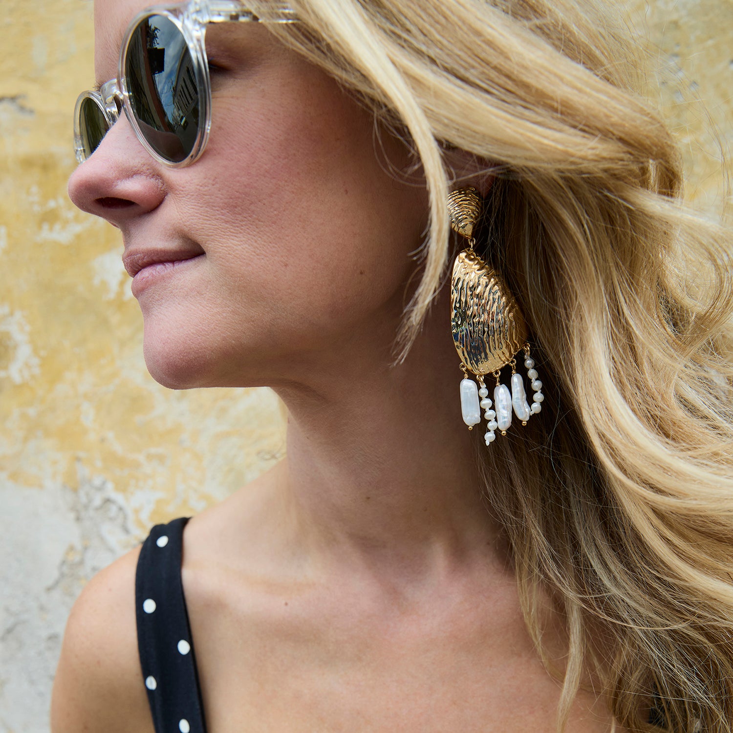 Model wearing Luxe Gloria Earrings against stone background. 