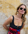Woman wearing Luxe Gloria Earrings, sunglasses and a polka dot dress against a textured wall.