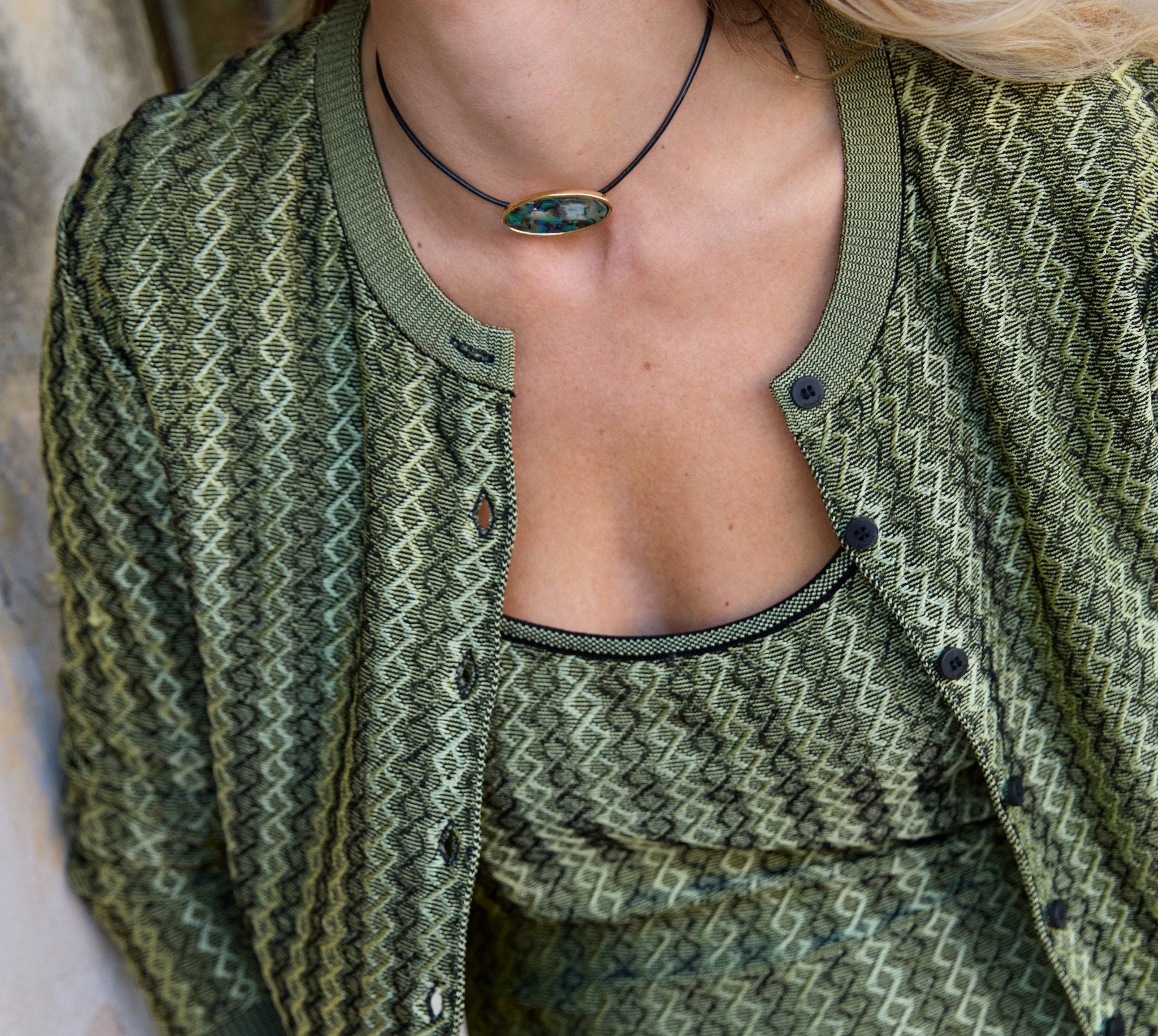 Green patterned cardigan worn by a person, with a focus on the neckline and chest area.