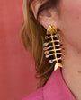 Fish shaped gold earrings on model against red background