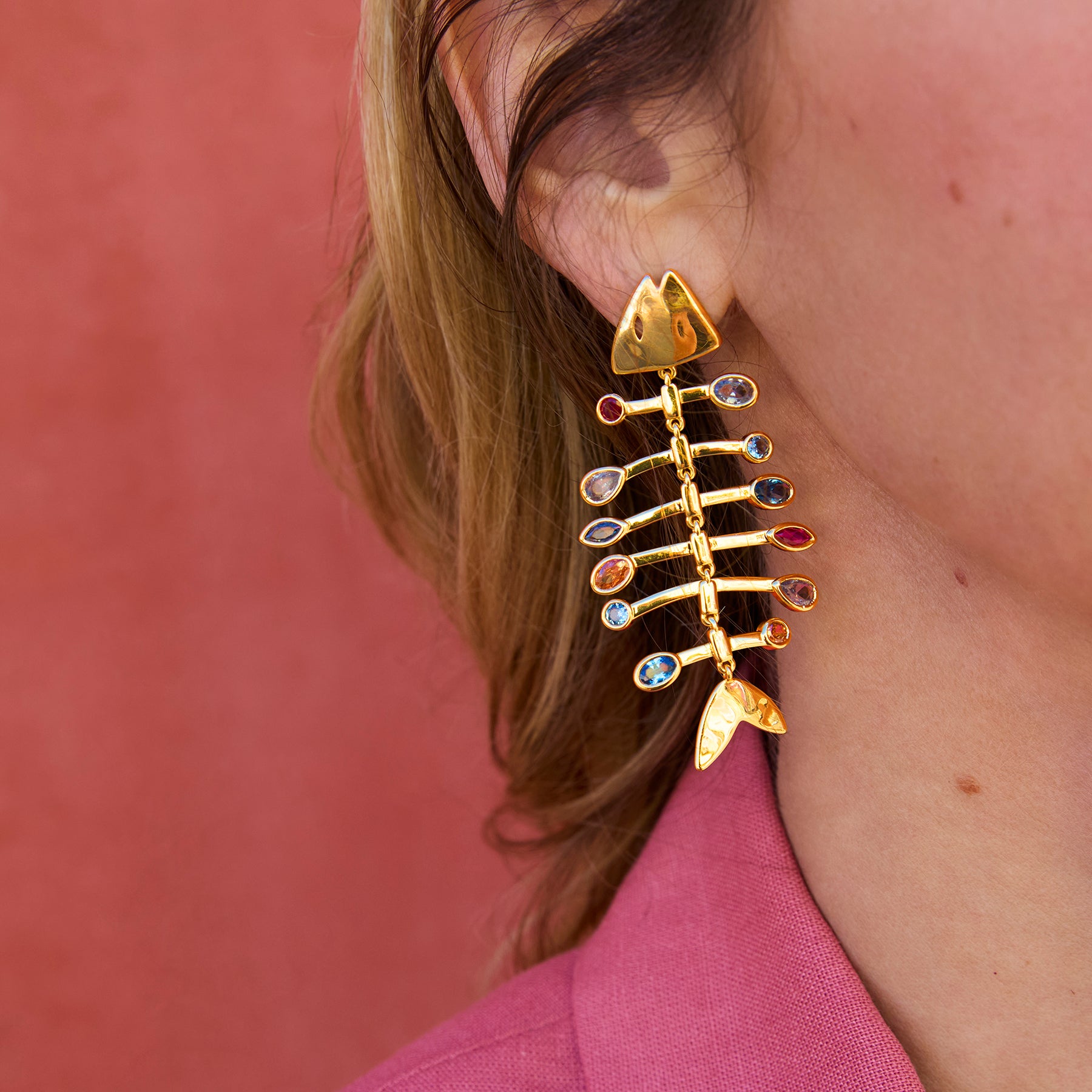 Fish shaped gold earrings on model against red background