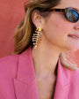 Woman wearing gold fishbone earrings and sunglasses with a pink background
