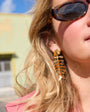 Close-up of a person wearing gold fishbone-shaped earrings with a blurred background