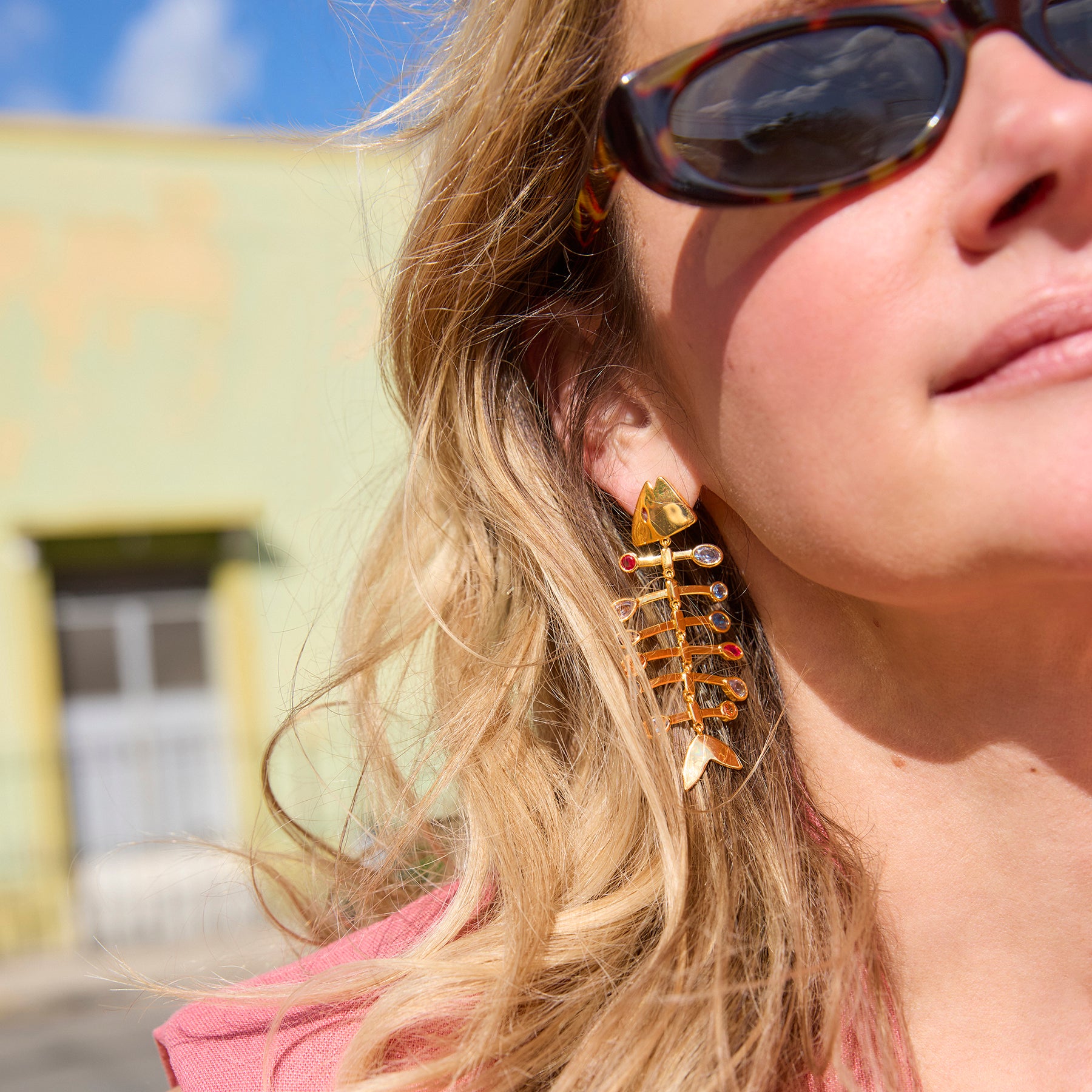 Close-up of a person wearing gold fishbone-shaped earrings with a blurred background