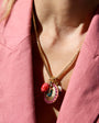 Close-up of a person wearing a gold necklace with colorful pendants against a pink background