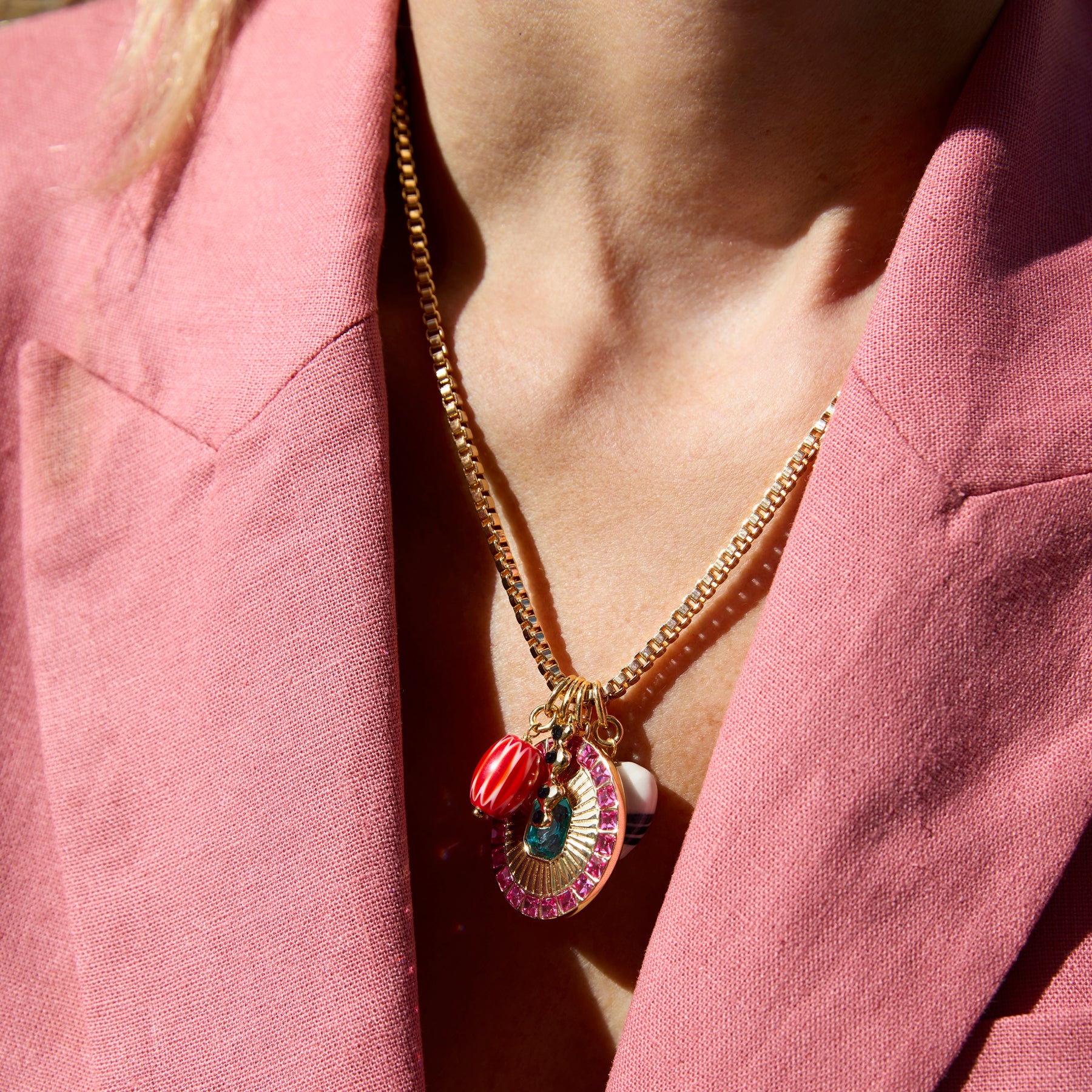 Close-up of a person wearing a gold necklace with colorful pendants against a pink background