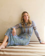 Woman sitting on a striped floor wearing a patterned dress.