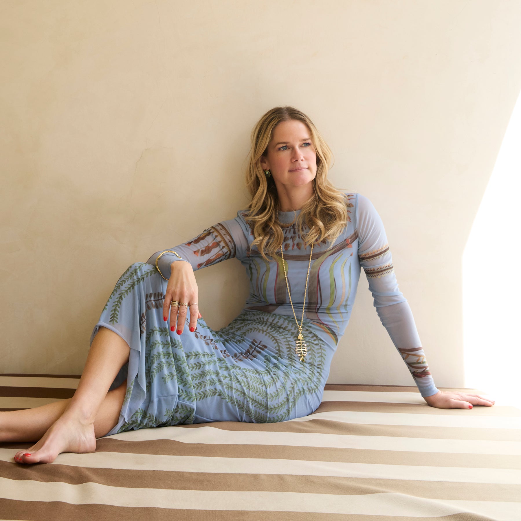 Woman sitting on a striped floor wearing a patterned dress.