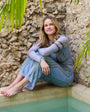 Woman sitting by a stone wall with greenery wearing a gold and blue glass stone cuff bracelet