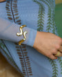 Gold bracelet and ring on a person wearing a light blue garment with leaf patterns.