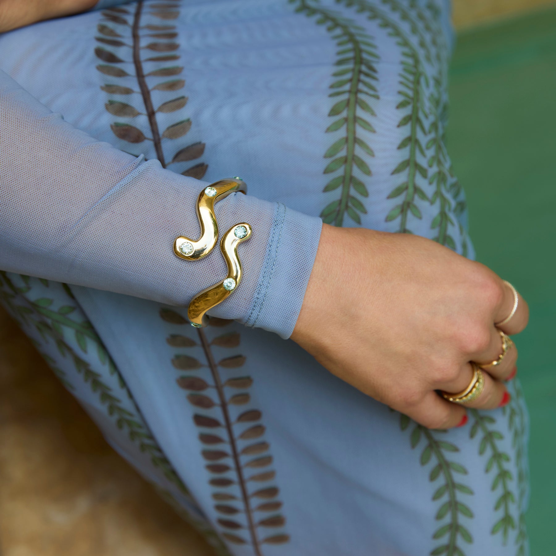 Gold bracelet and ring on a person wearing a light blue garment with leaf patterns.