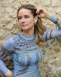 Model wearing blue dress with long gold necklace against rocky wall