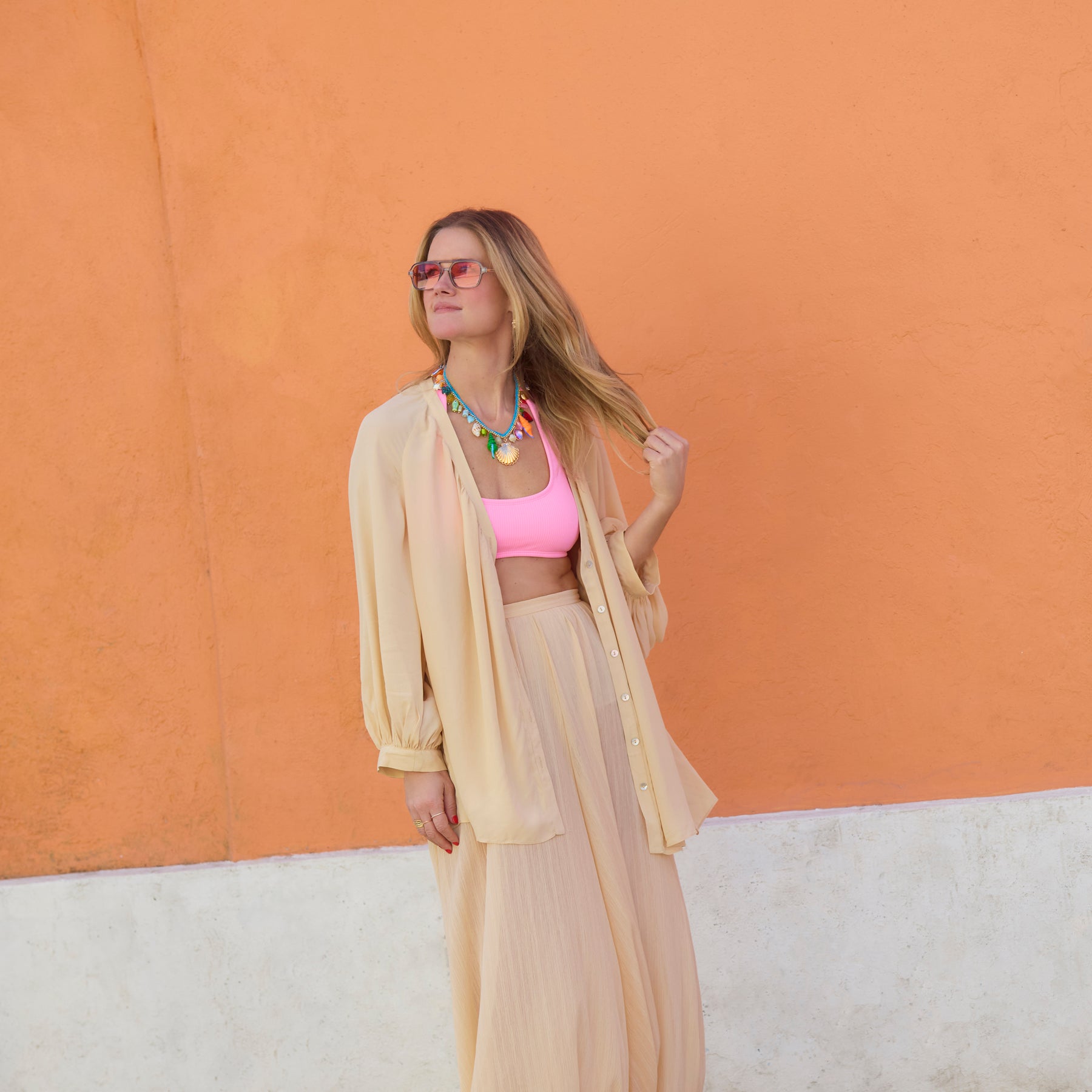 Model wearing colorful shell necklace in peach set with orange background