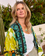 Woman wearing a colorful patterned jacket outdoors with plants in the background