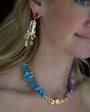 Close-up of a woman wearing a blue beaded necklace and gold earrings with a red gemstone.