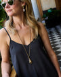 Woman wearing sunglasses and a black dress in an outdoor setting with plants and checkered floor.