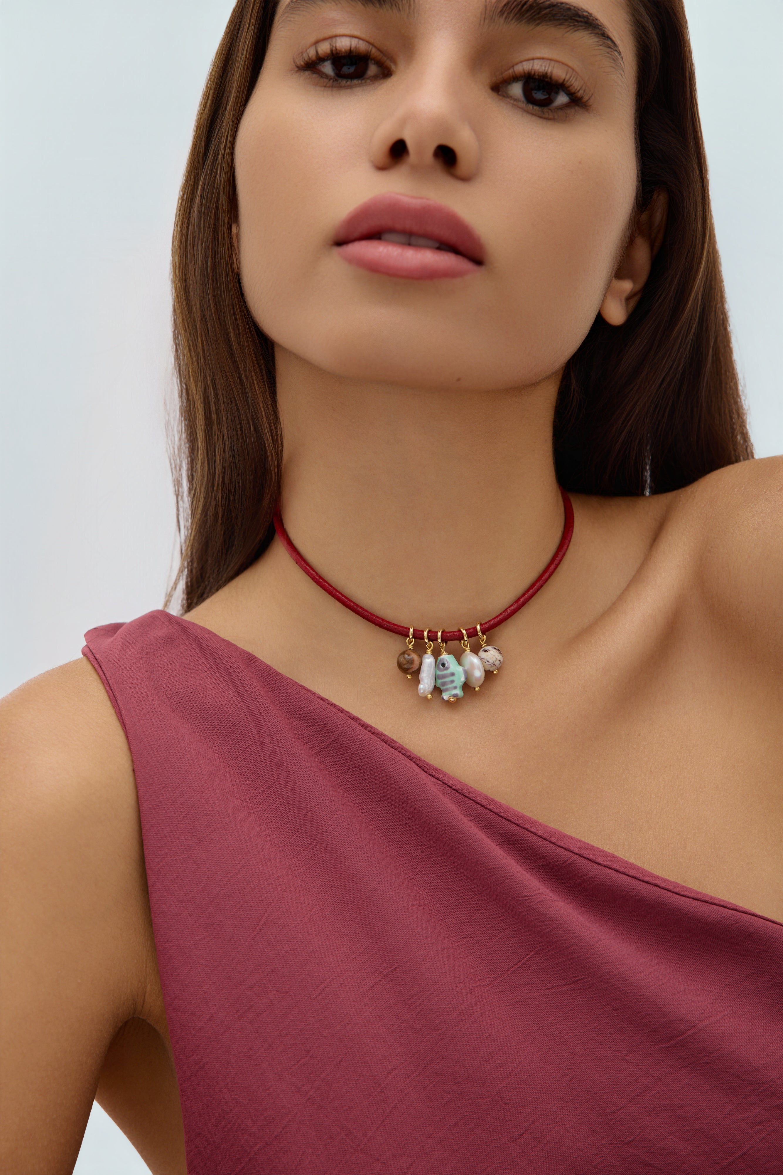 Woman wearing a red choker necklace with small pendants against a plain background