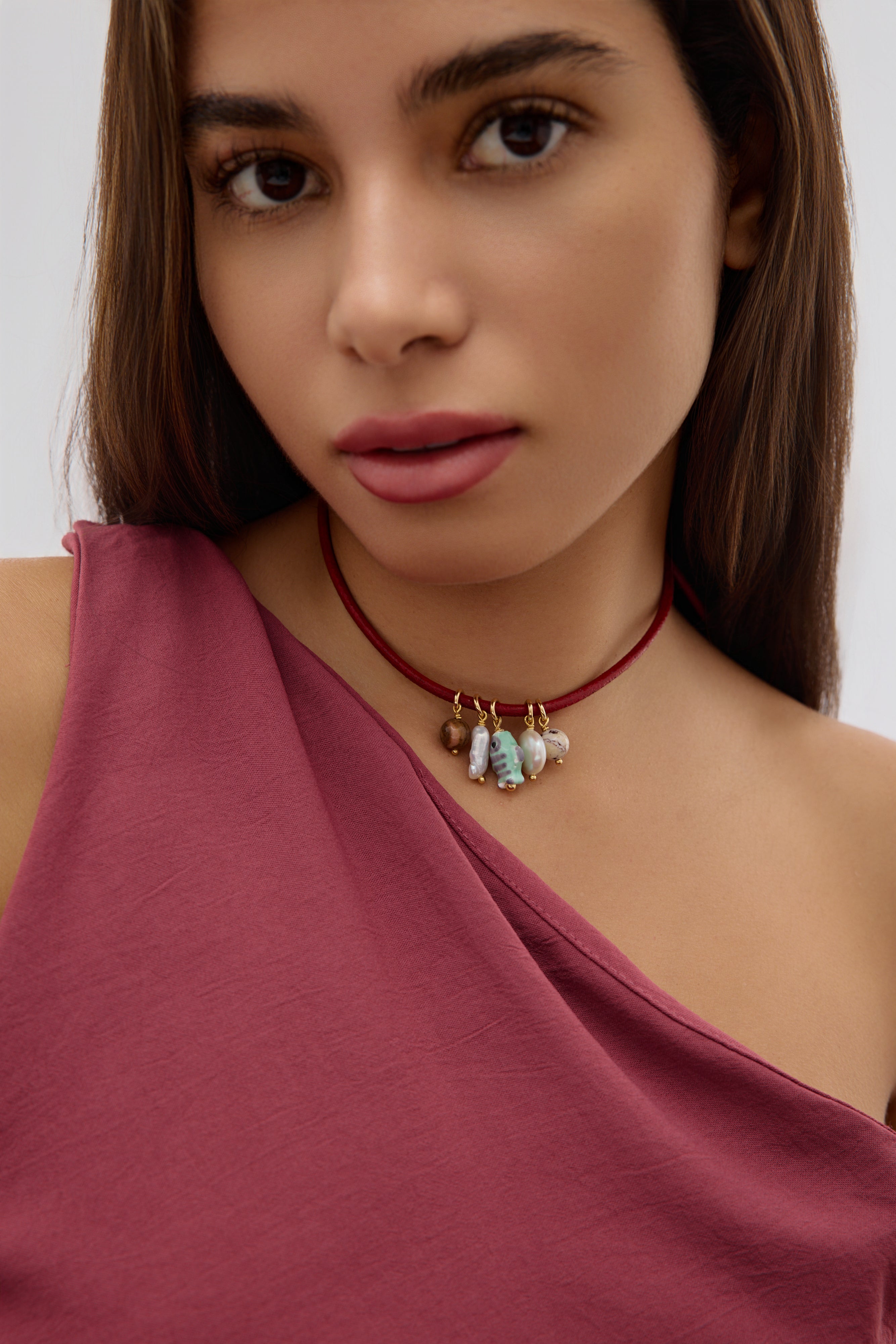 Woman wearing a one-shoulder top and a necklace with pendants against a white background
