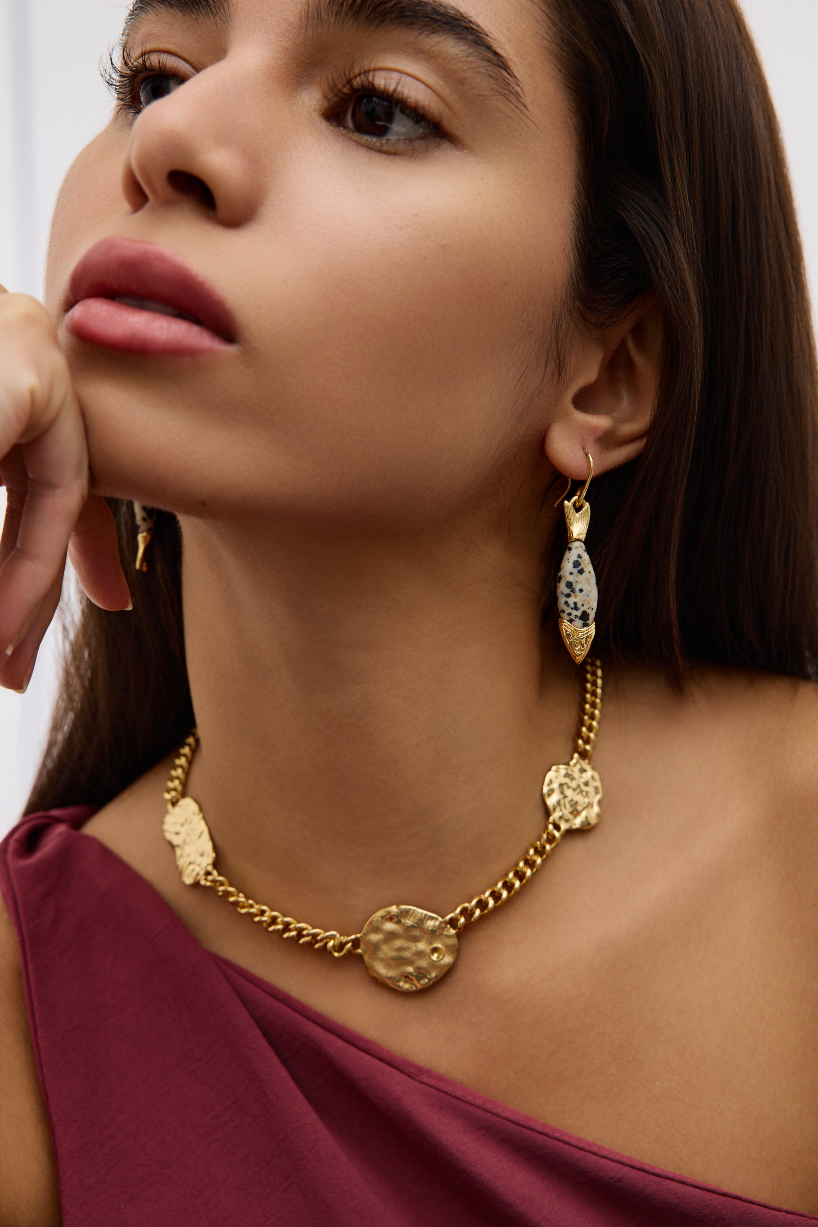 Woman wearing a gold necklace and earrings on a plain background