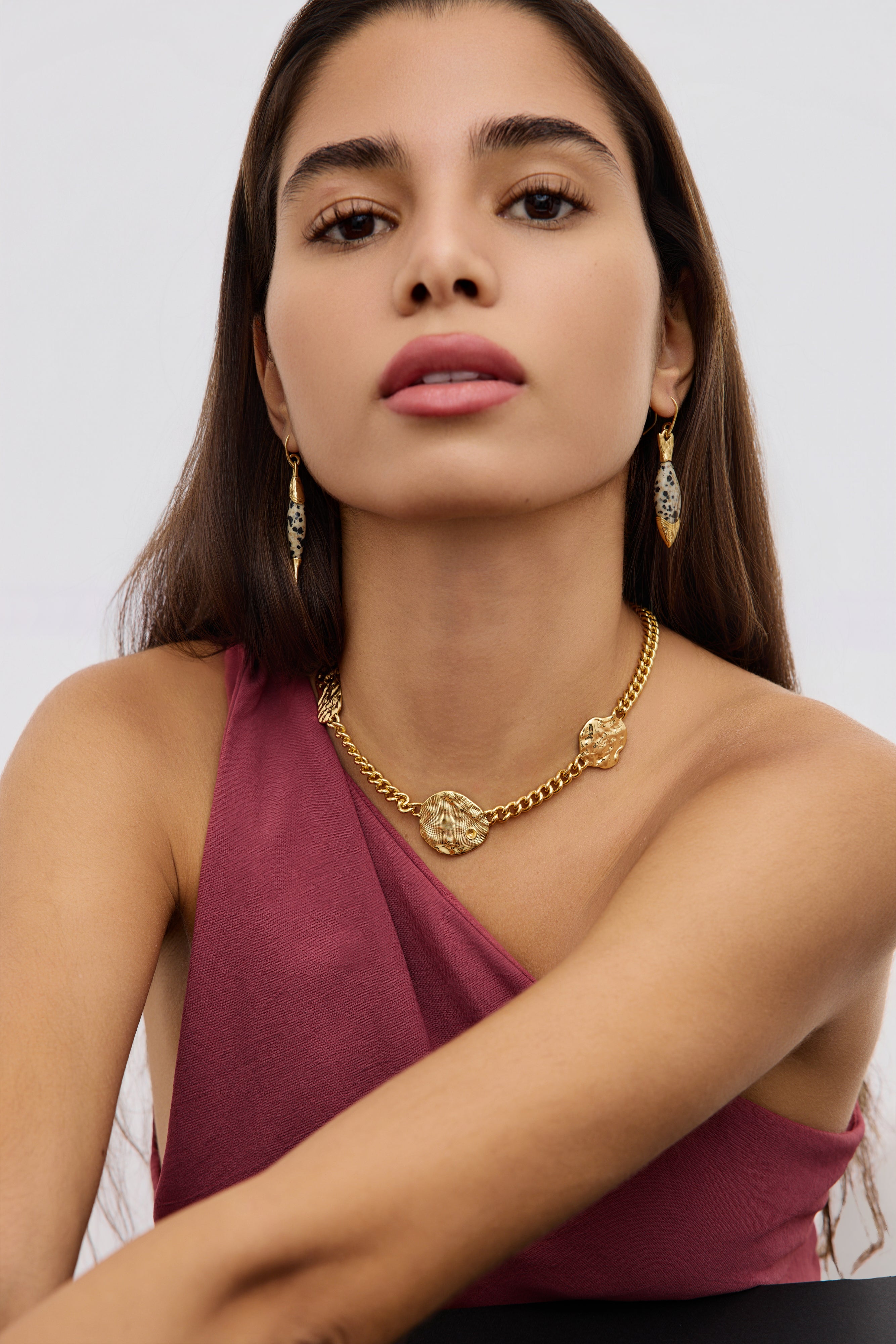 Woman wearing a gold necklace and earrings against a white background