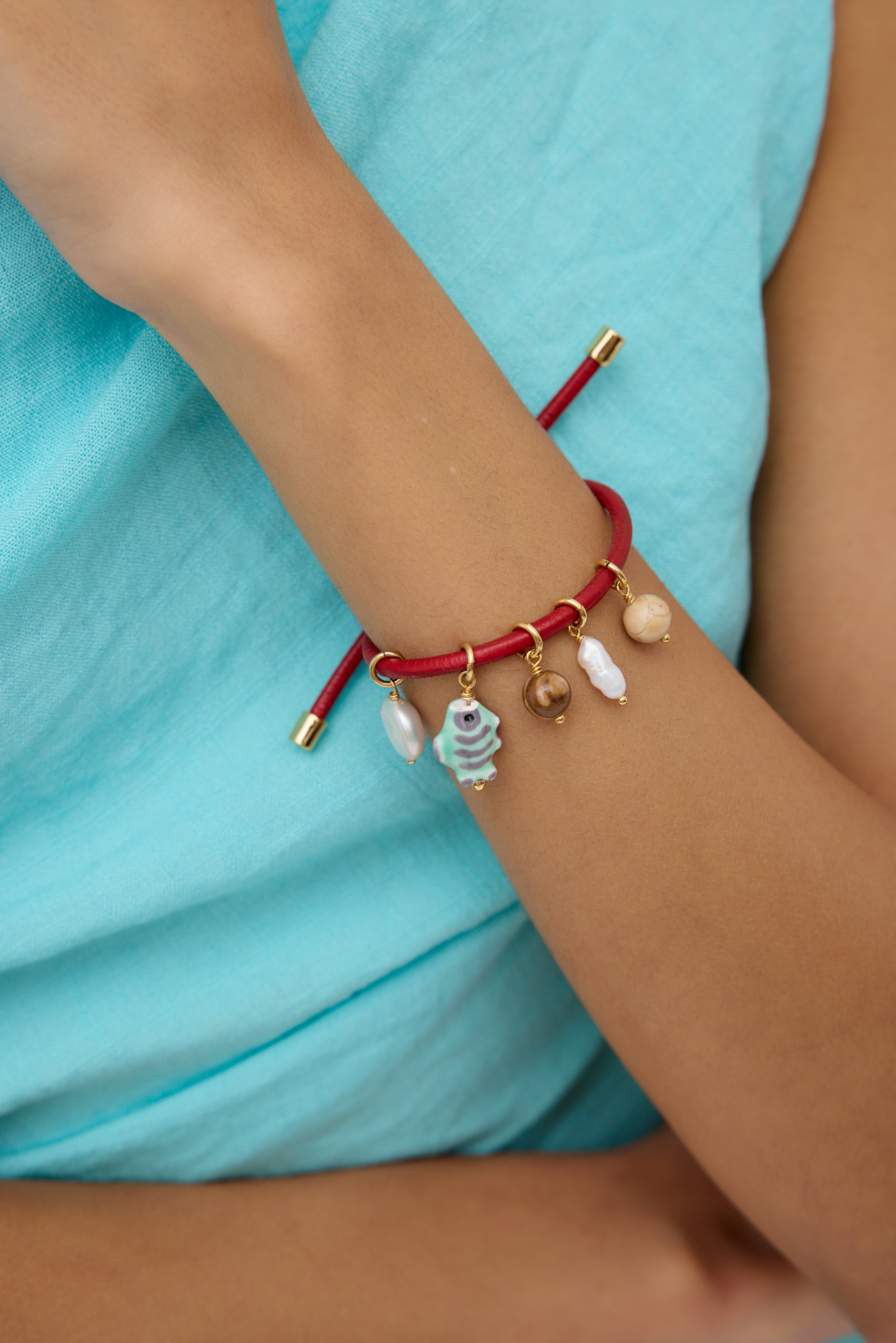 Red bracelet with charms on a wrist against a turquoise fabric background