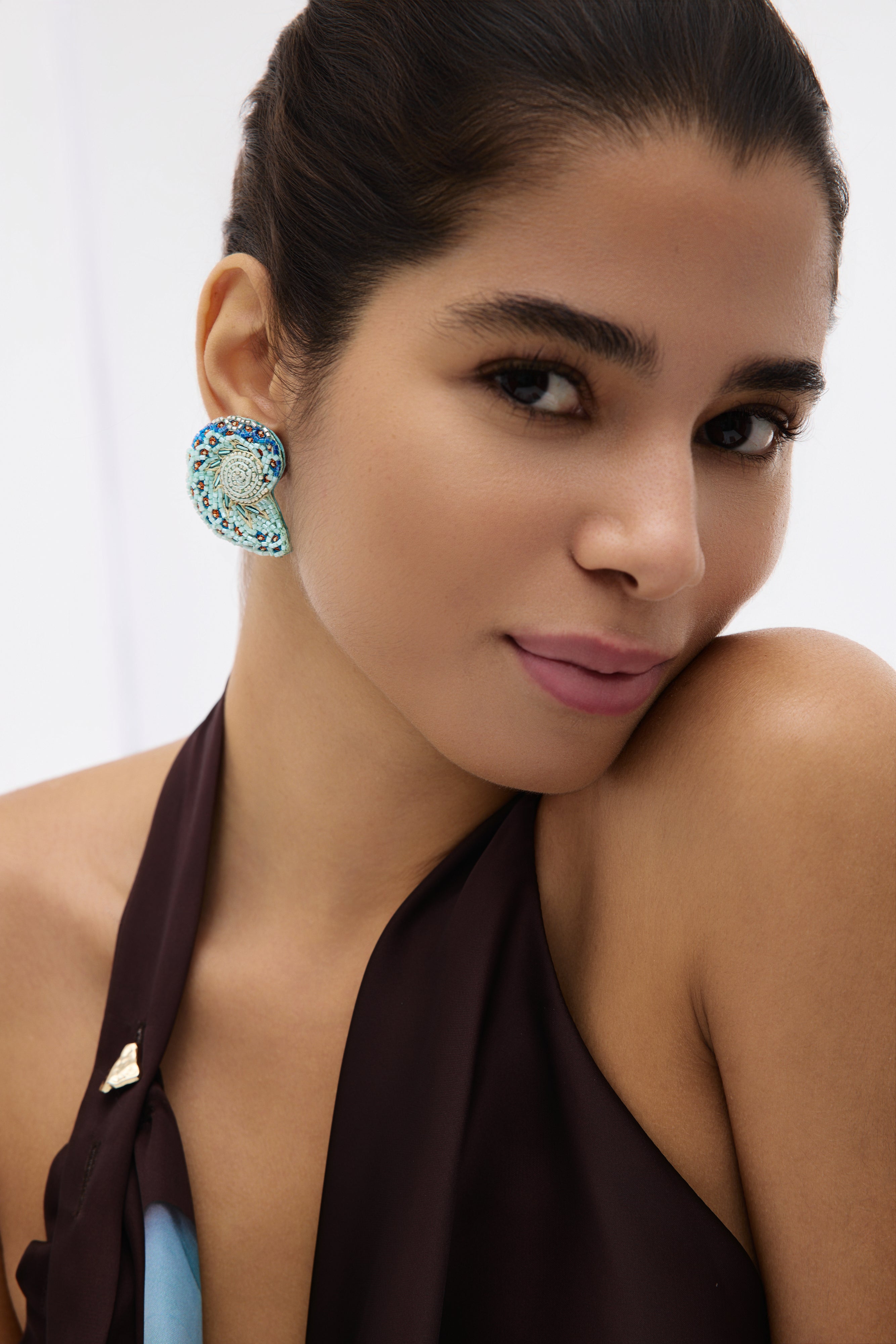 Woman wearing a blue earrings and brown top with a blurred background