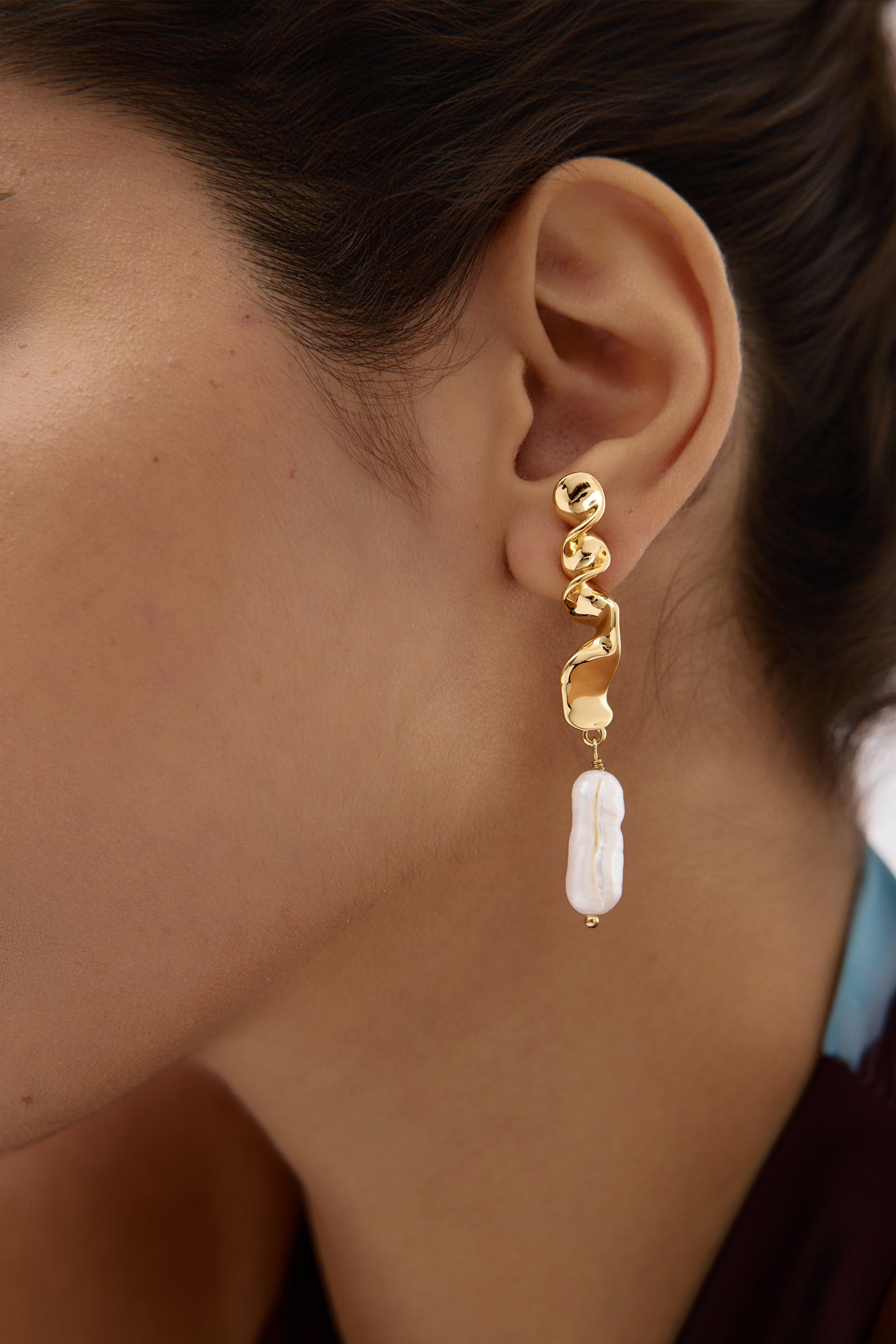 Gold earring with a white pearl drop worn by a person