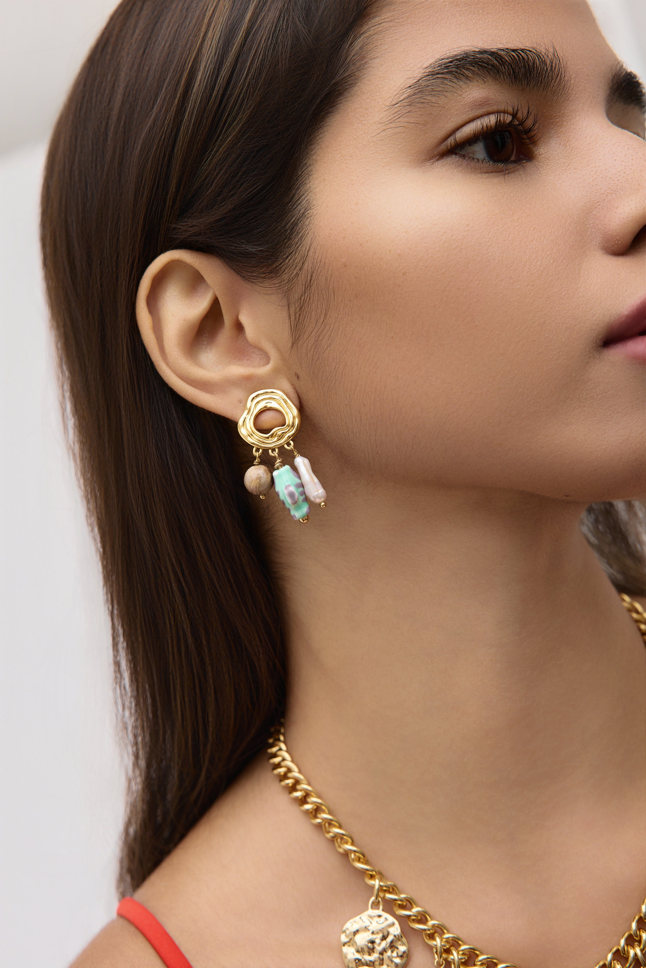 Close-up of a woman wearing gold earrings and a necklace on a white background