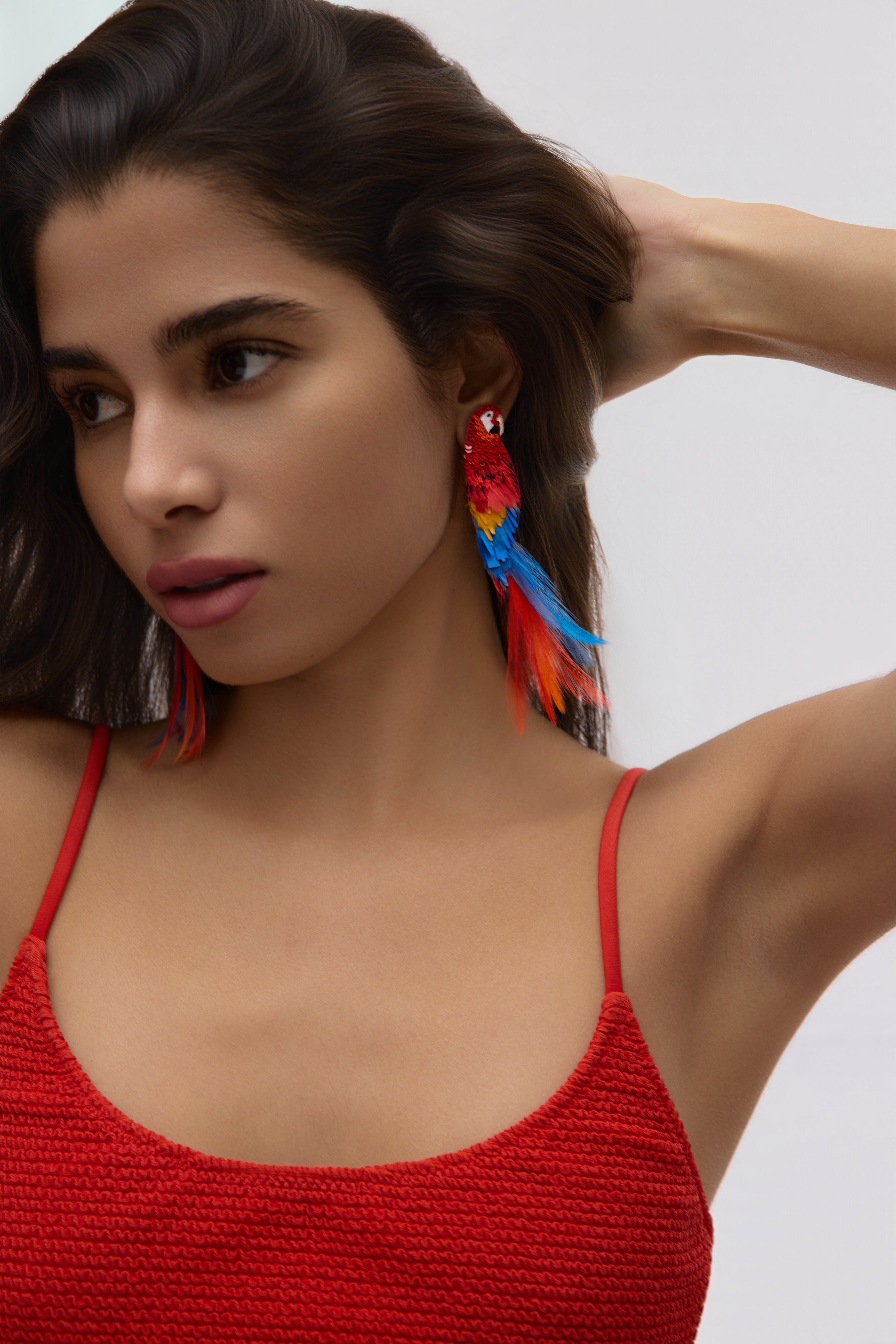 Woman wearing colorful earrings and a red top against a white background