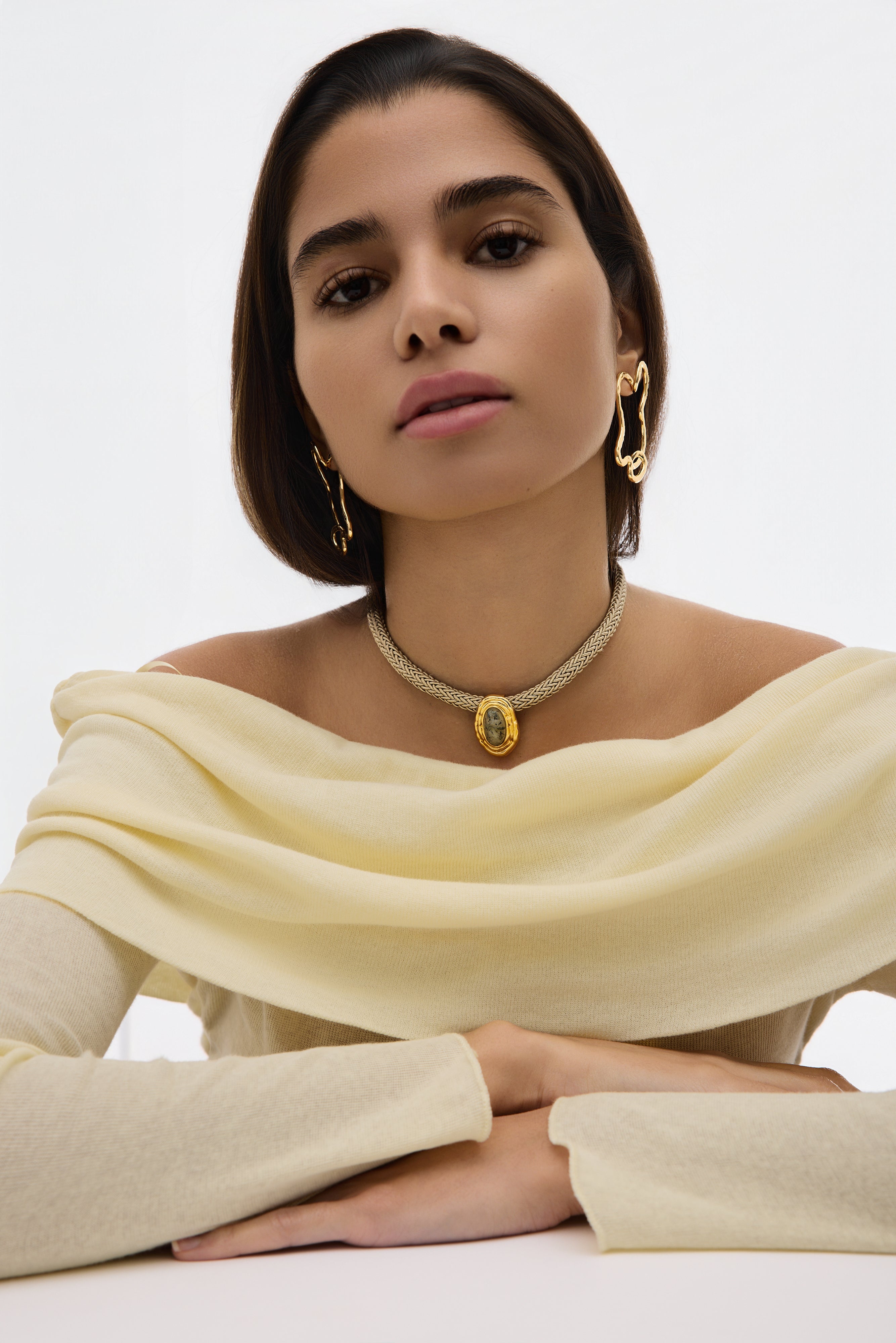 Woman wearing a yellow off-shoulder top and gold jewelry against a white background