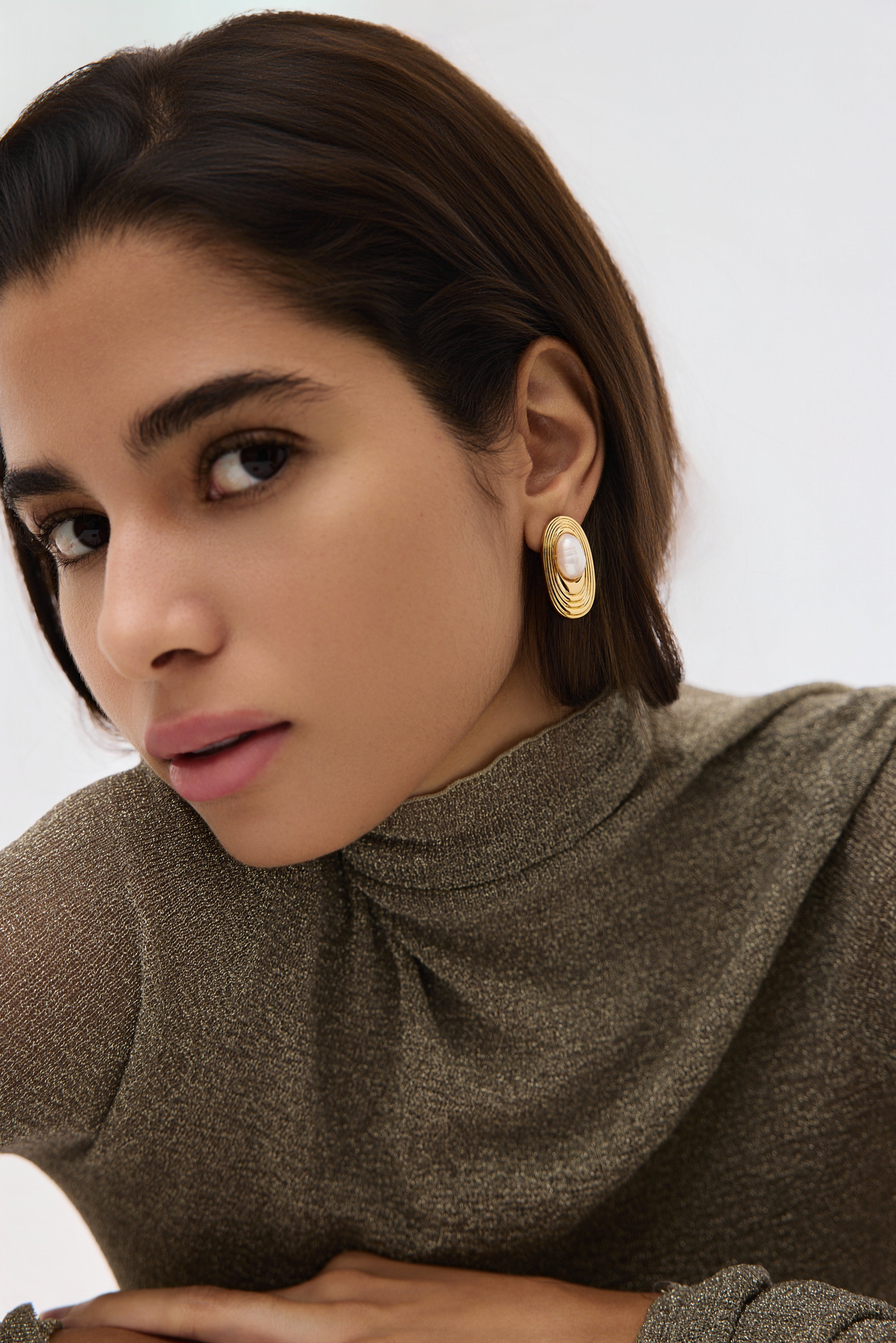 Woman wearing gold earrings with a pearl center on a neutral background