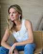 Woman sitting on a chair wearing a white top and blue jeans, with a neutral background.