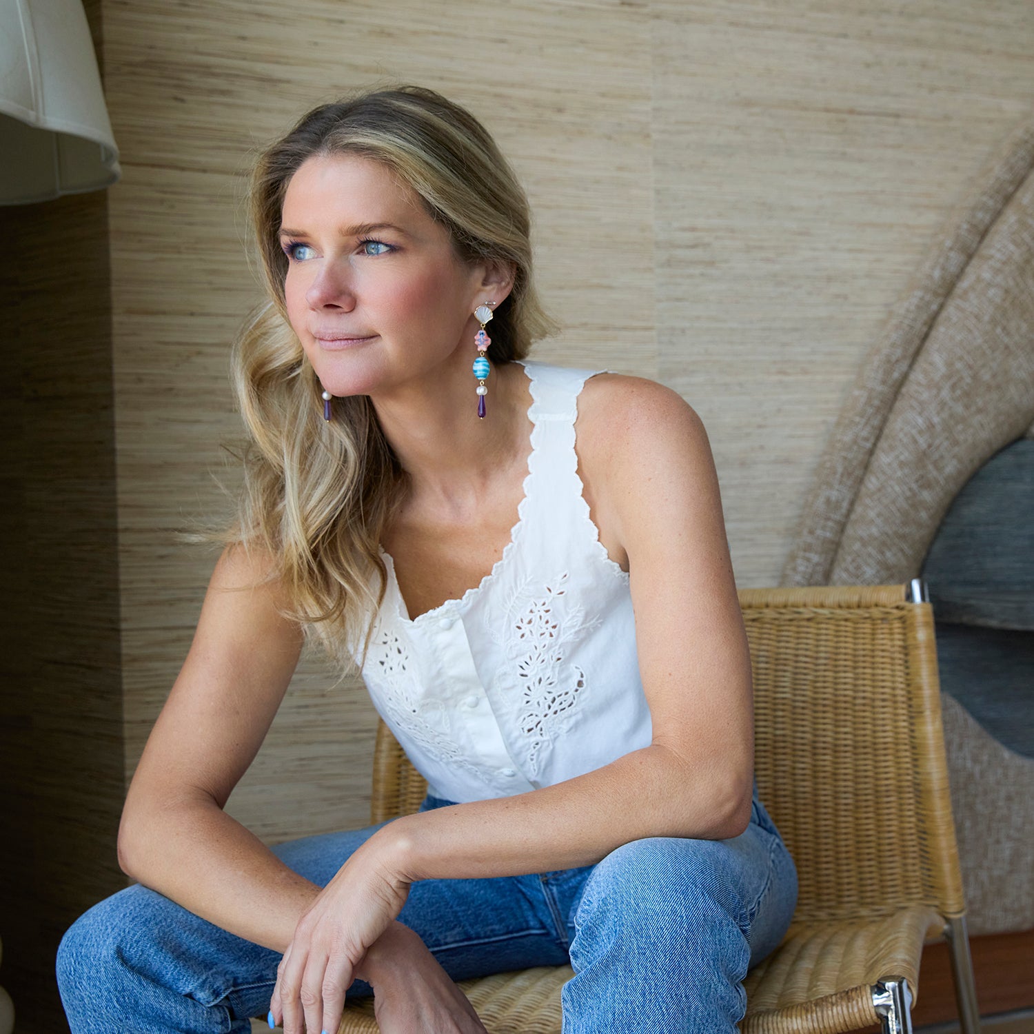 Woman sitting on a chair wearing a white top and blue jeans, with a neutral background.