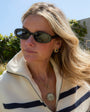 Woman wearing sunglasses and gold stud earrings with a white sweater with blue stripes outdoors