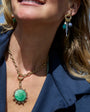Close-up of a woman wearing a gold necklace with a green pendant and matching earrings.