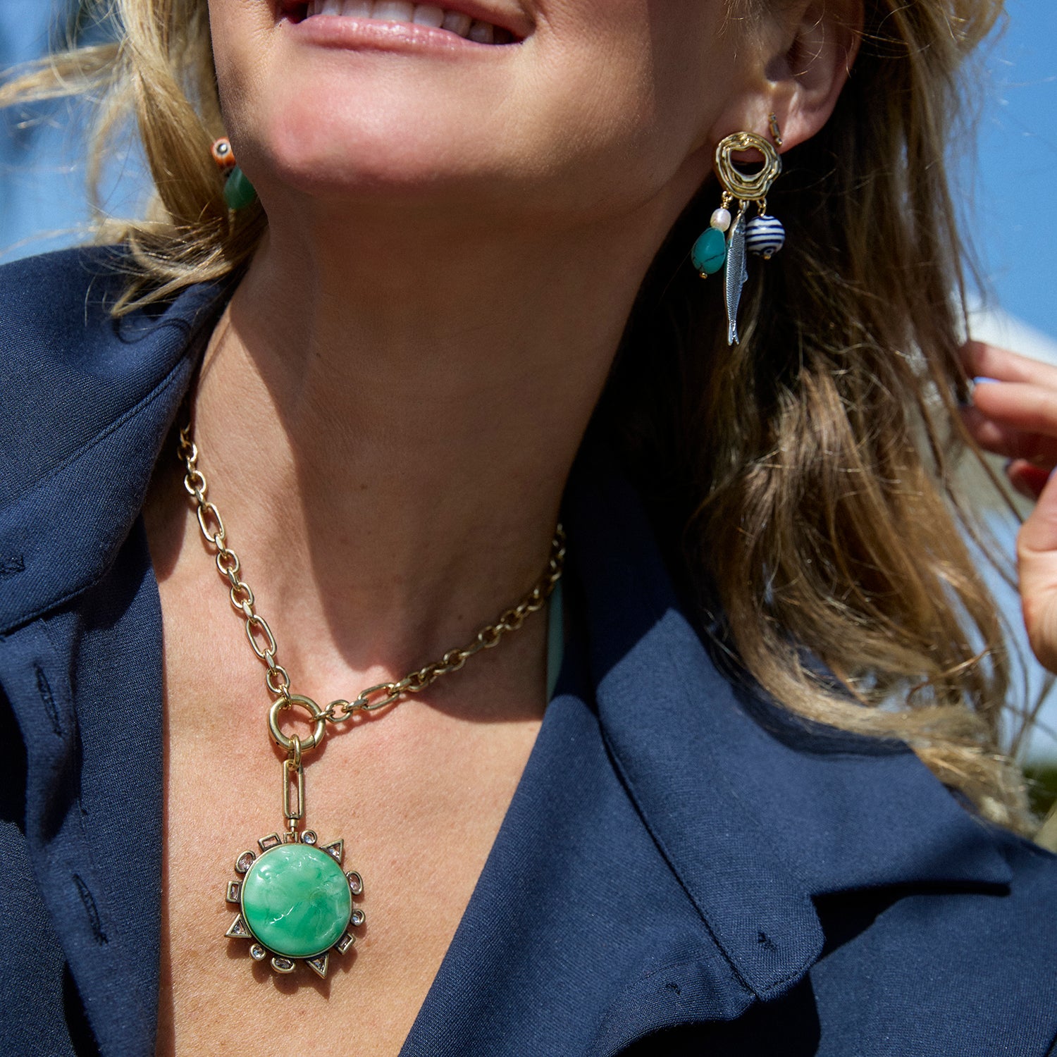 Close-up of a woman wearing a gold necklace with a green pendant and matching earrings.