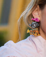 Close-up of a person wearing colorful fish-shaped earrings with a blurred background.