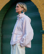 Woman in a light jacket standing in front of a yellow wall with an archway wearing fish shaped embroidered earrings