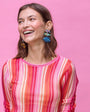 Woman wearing a colorful striped shirt with fish shaped colorful beaded earrings against a pink background