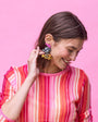 Woman wearing a colorful striped shirt with fish shaped colorful beaded earrings against a pink background