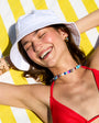Woman in a red bikini and white sun hat with a colorful beaded collar necklace lying on a yellow and white striped towel.